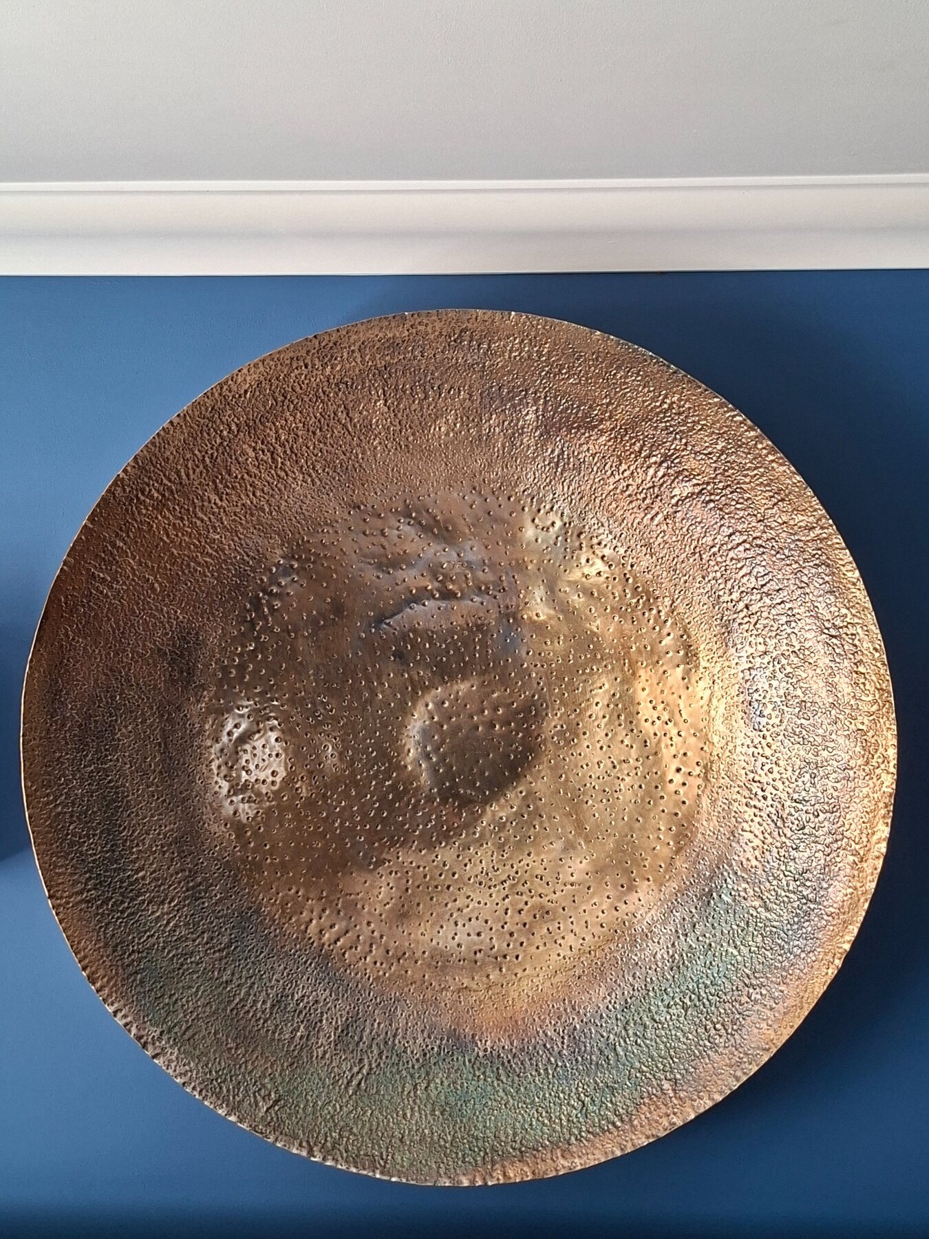 Textured bronze artwork against a rich blue wall
